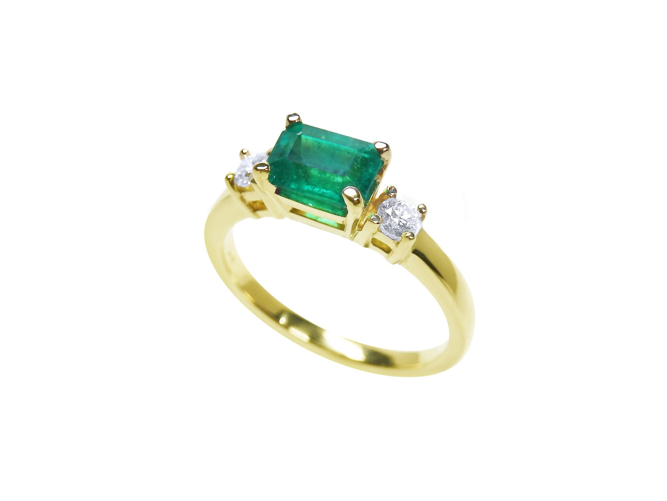 A partial lateral view of a rectangular colombian emerald with side diamonds in yellow gold.