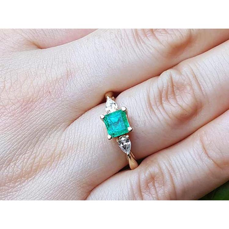 A natural colombian emerald square cut and side diamonds ring on a hand.
