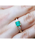 A natural colombian emerald square cut and side diamonds ring on a hand.