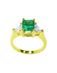 A center natural colombian emerald ring for women, flanked by trillion cut diamonds in 18 yellow gold.
