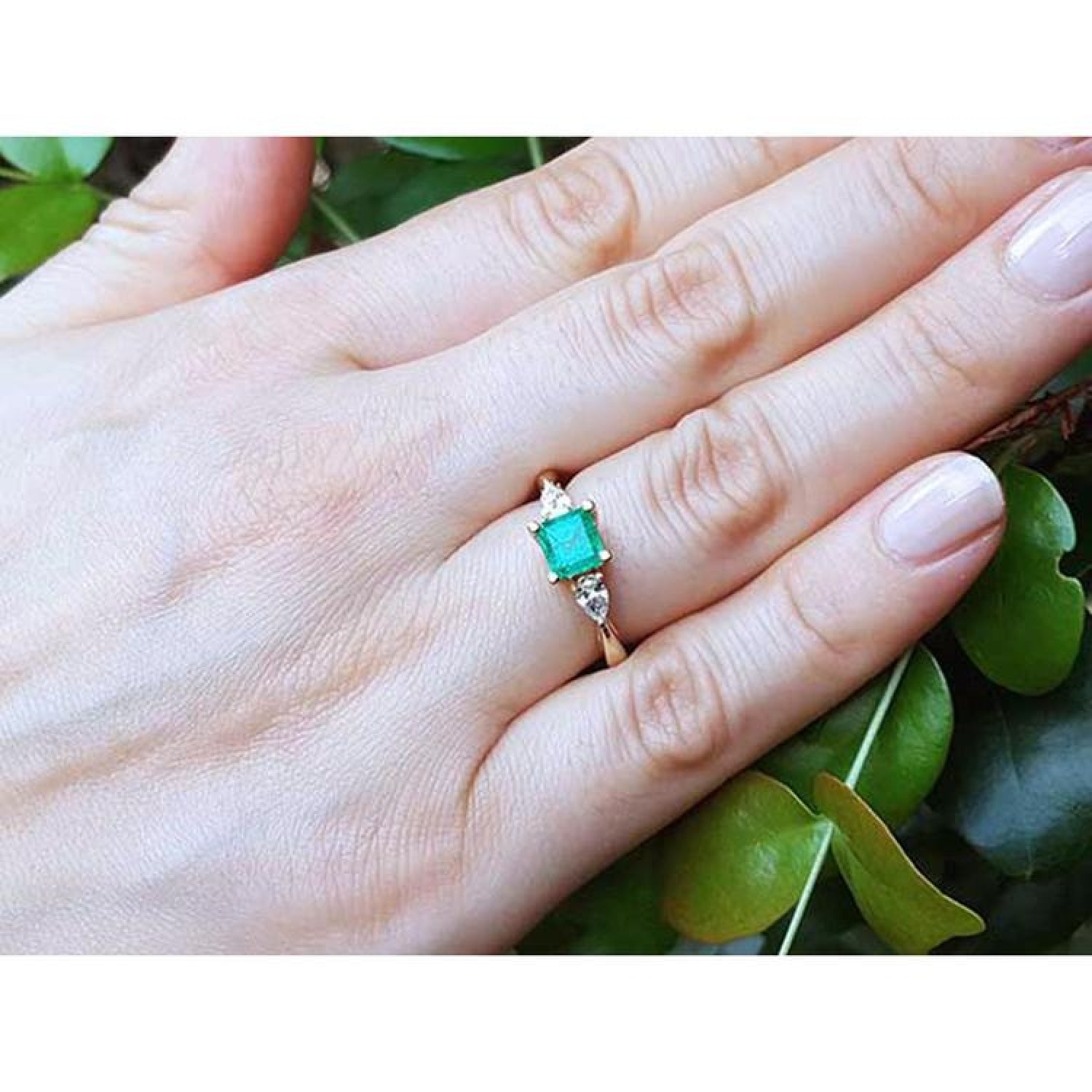 14K yellow gold three-stone emerald ring with pear-shaped side diamonds on a hand.