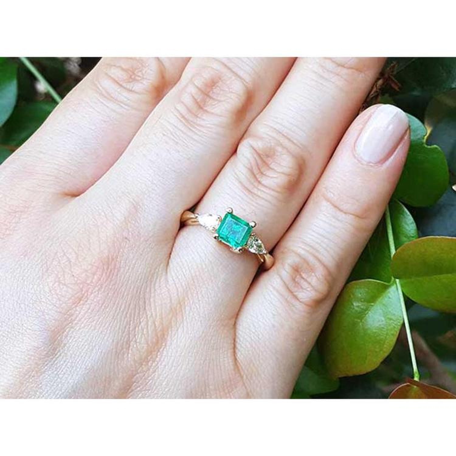14K yellow gold three-stone emerald ring with pear-shaped side diamonds on a hand.