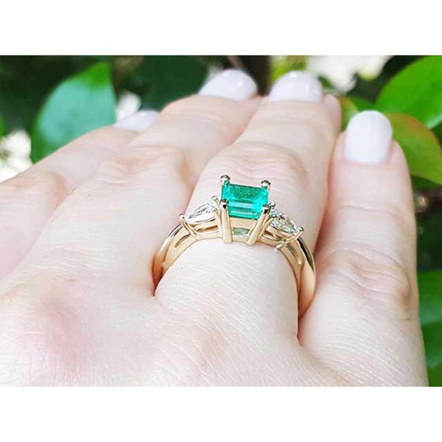 14K yellow gold three-stone ring with vibrant emerald and pear-shaped side diamonds on a hand.