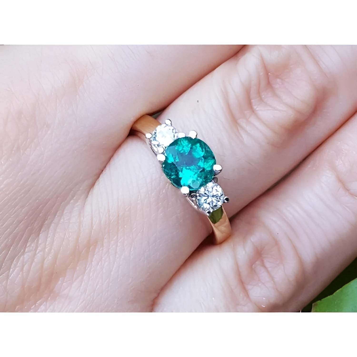 A women's round cut colombian emerald three stone ring with side natural diamonds on a finger.