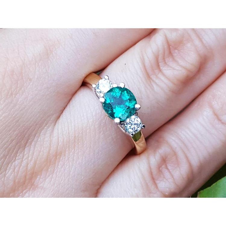 A women's round cut colombian emerald three stone ring with side natural diamonds on a finger.