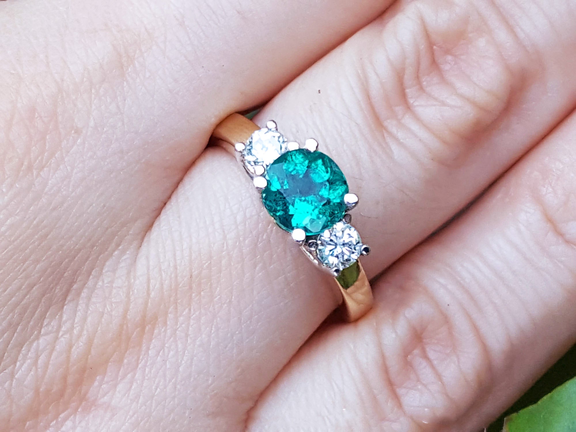 A women's emerald three stone ring side diamonds on a finger.
