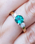 A women's emerald three stone ring side diamonds on a finger.