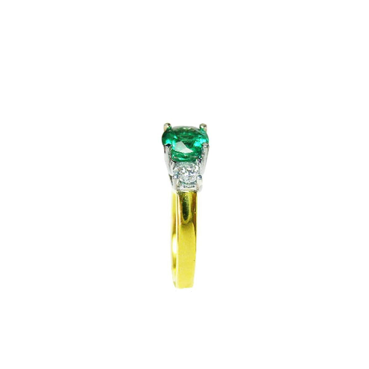 A side profile of this gold ring with a round emerald and smaller diamonds on a white background.
