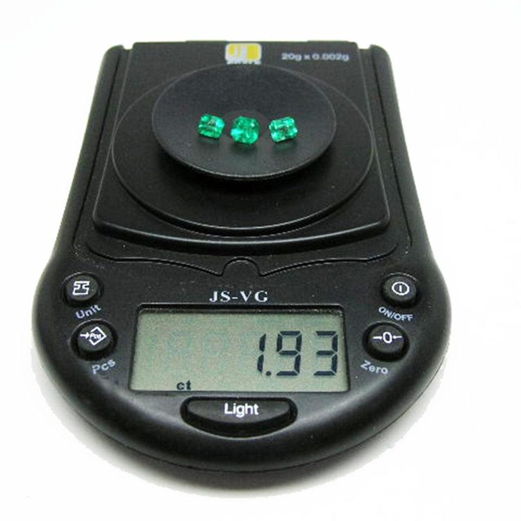 Three emerald-cut natural green emeralds on a black digital scale displaying 1.93 ct.