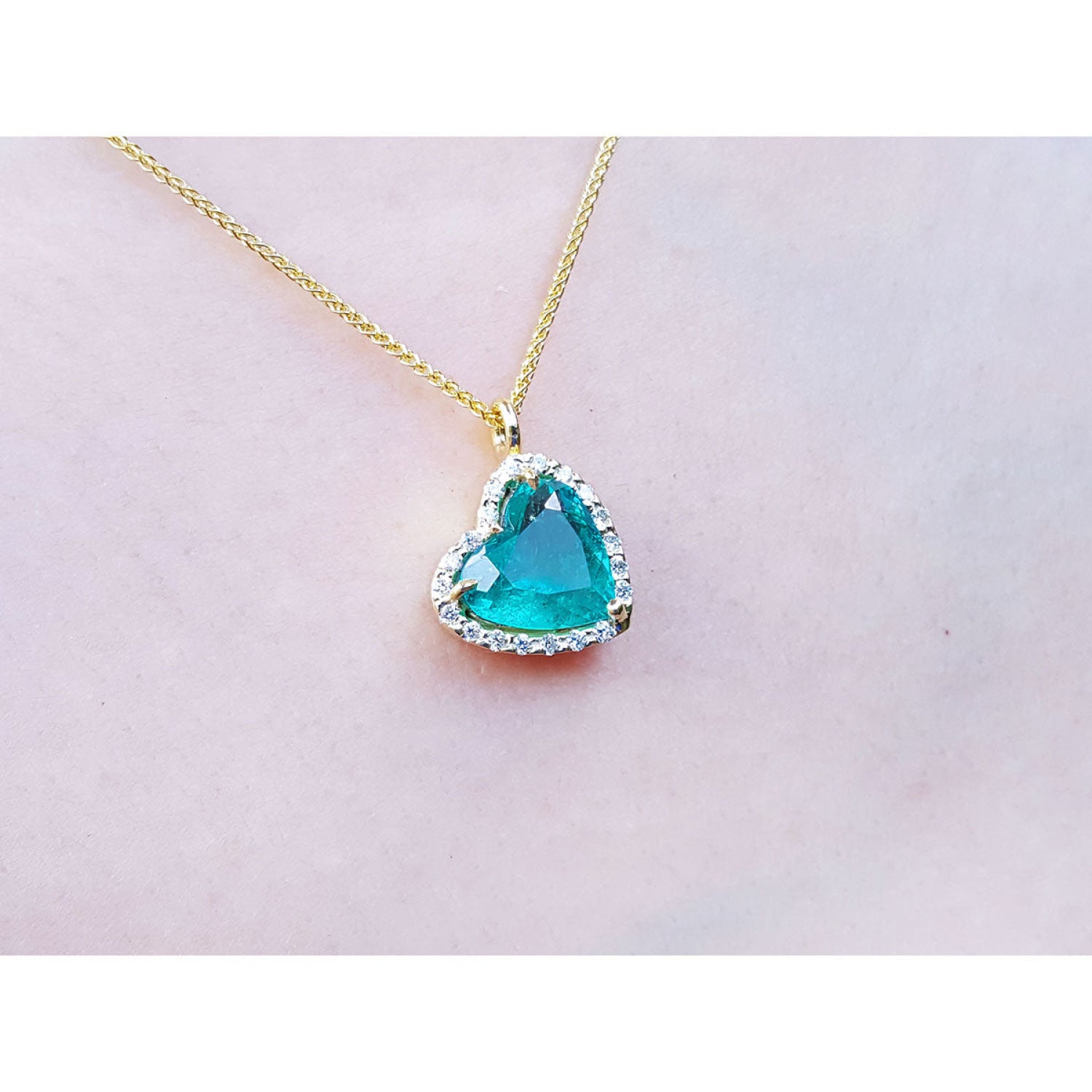 Tilted heart emerald pendant with halo diamonds on an 18K yellow gold chain.