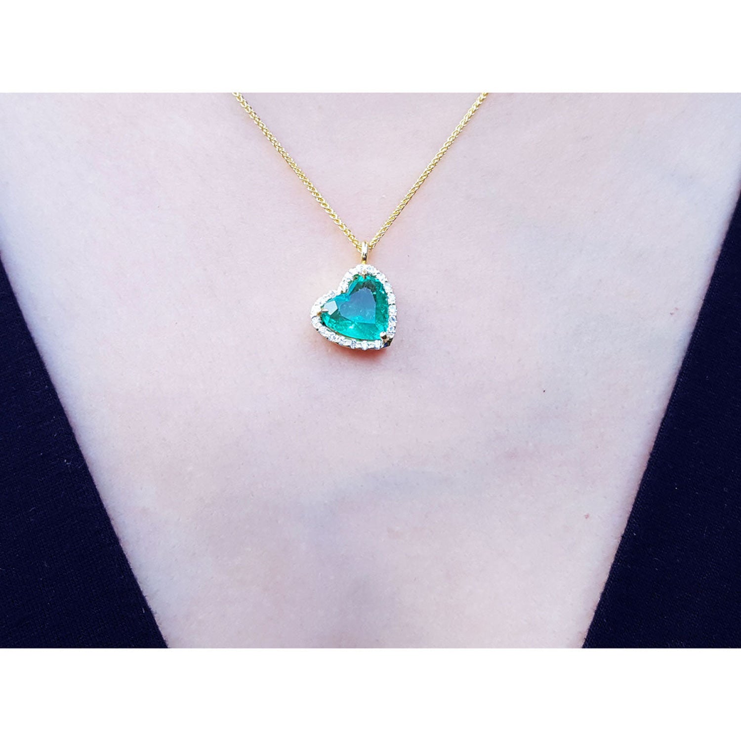Tilted heart emerald necklace with halo diamonds on an 18K yellow gold chain.