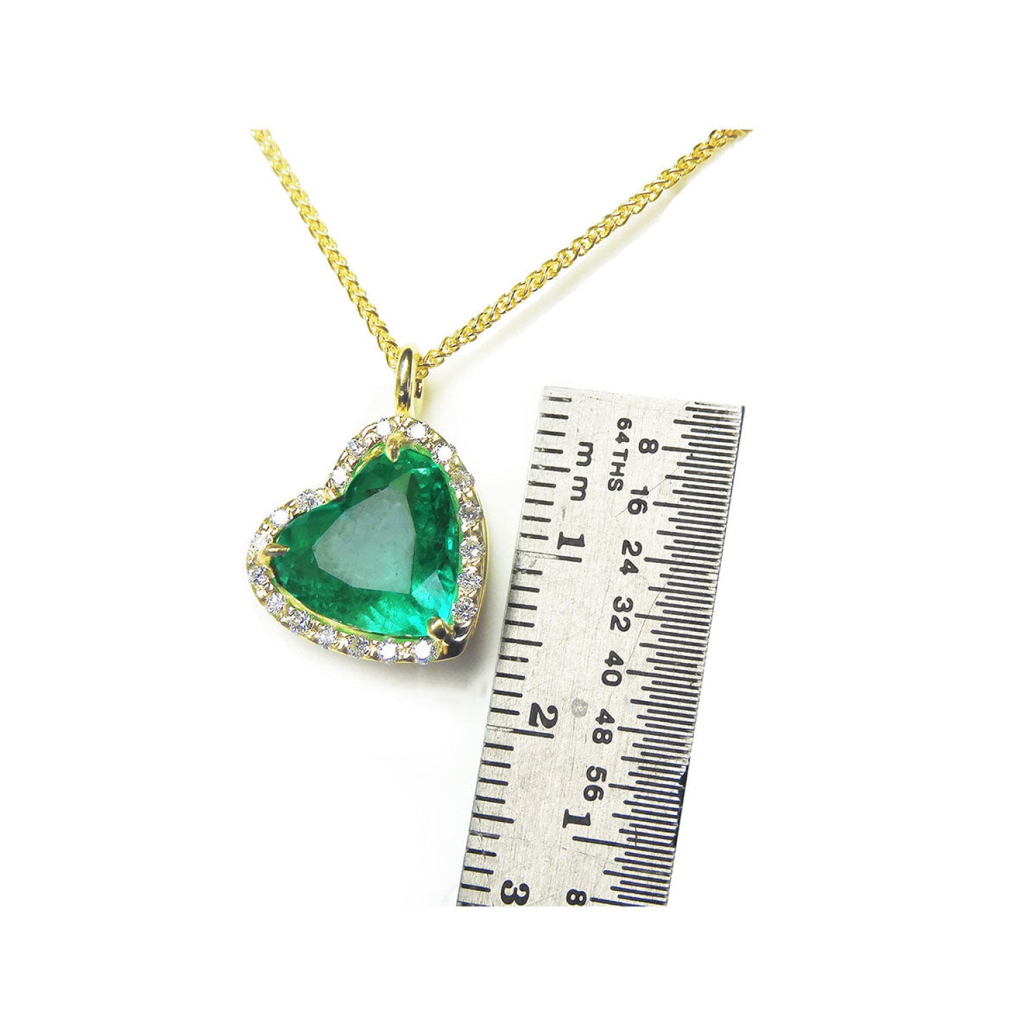 Tilted heart emerald necklace with halo diamonds on an 18K gold chain, shown with a ruler for scale.