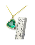 Tilted heart emerald necklace with halo diamonds on an 18K gold chain, shown with a ruler for scale.