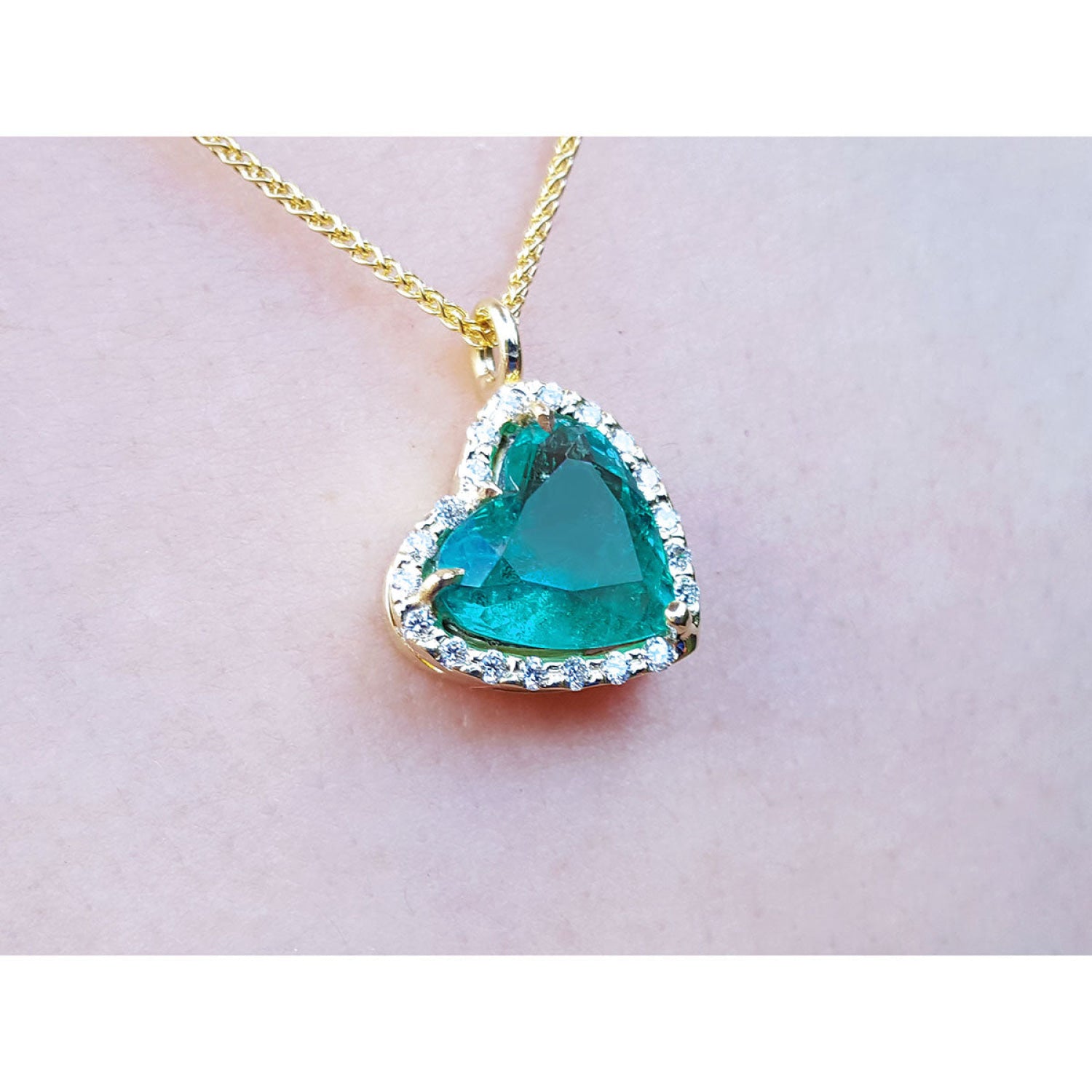 Tilted heart Colombian emerald necklace with halo diamonds on an 18K yellow gold chain.