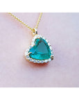 Tilted heart Colombian emerald necklace with halo diamonds on an 18K yellow gold chain.