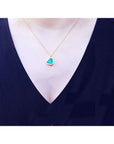 Tilted heart emerald necklace with halo diamonds on an 18K gold chain, worn on a woman's neck.