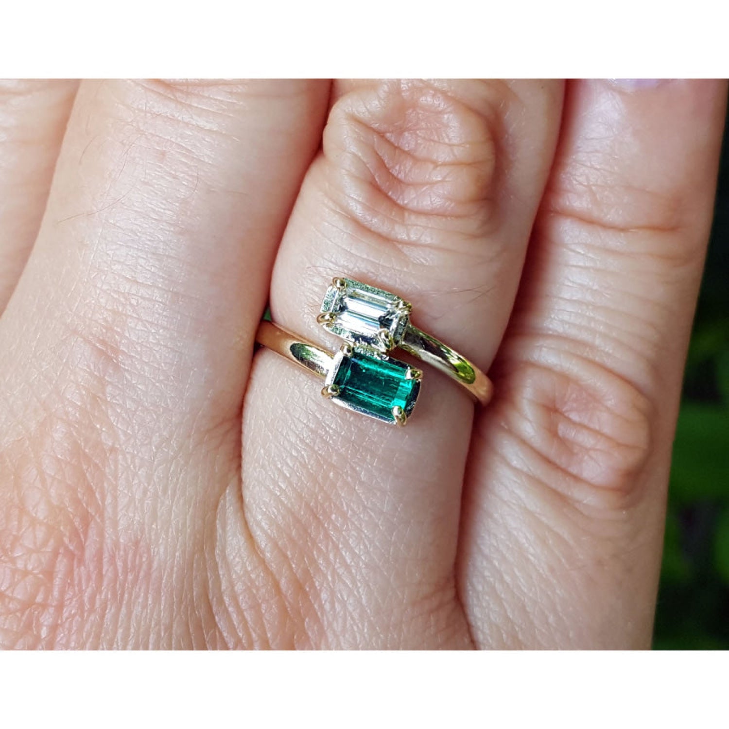 A close-up of a gold ring with two emerald-cut green gemstones worn on a person's finger.