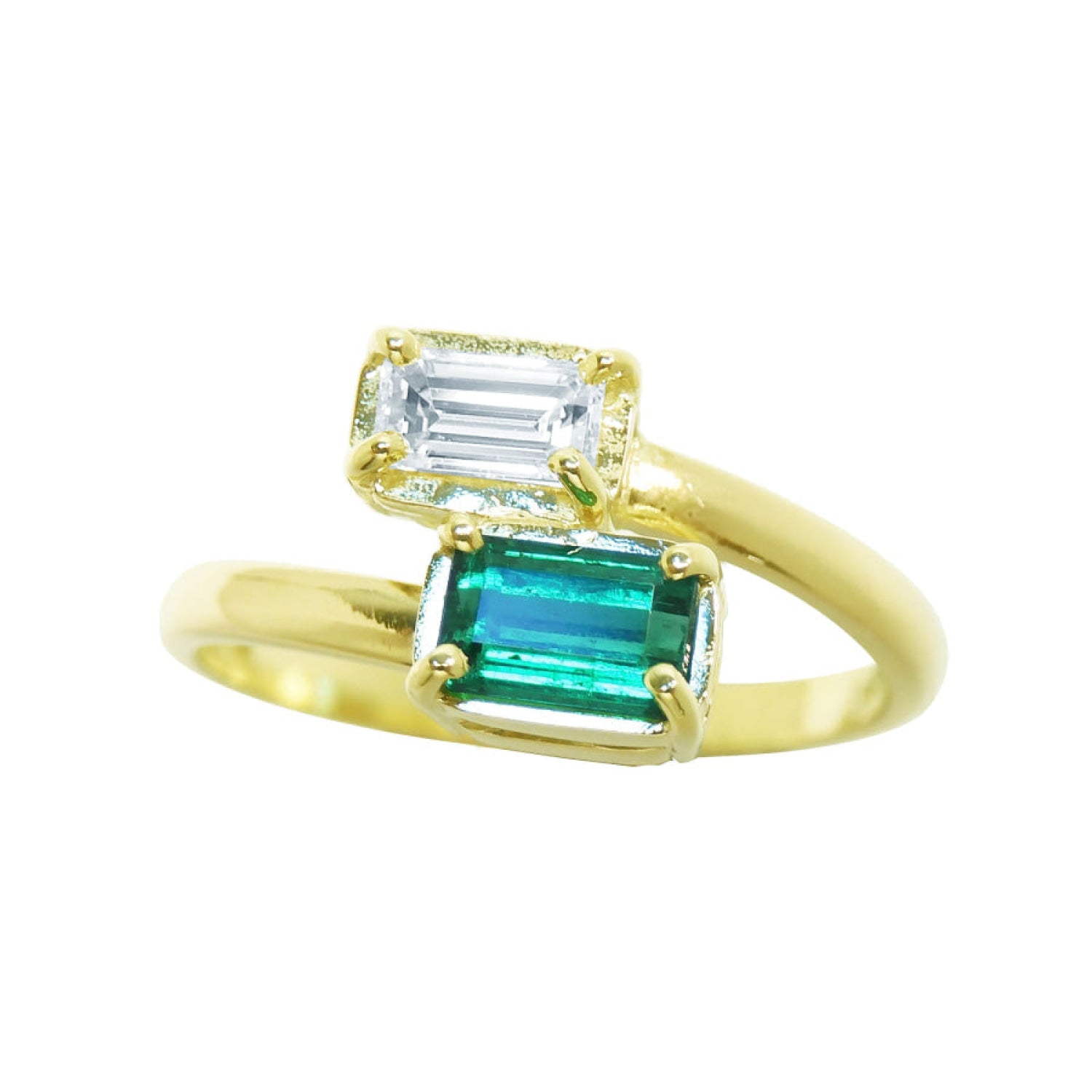 A yellow gold ring featuring two emerald-cut gemstones, with a larger green emerald and a smaller clear baguette stone above it, set against a plain white background.