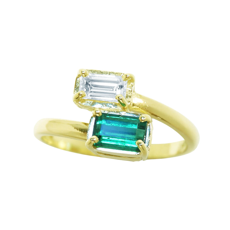 A yellow gold ring featuring two emerald-cut gemstones, with a larger green emerald and a smaller clear baguette stone above it, set against a plain white background.