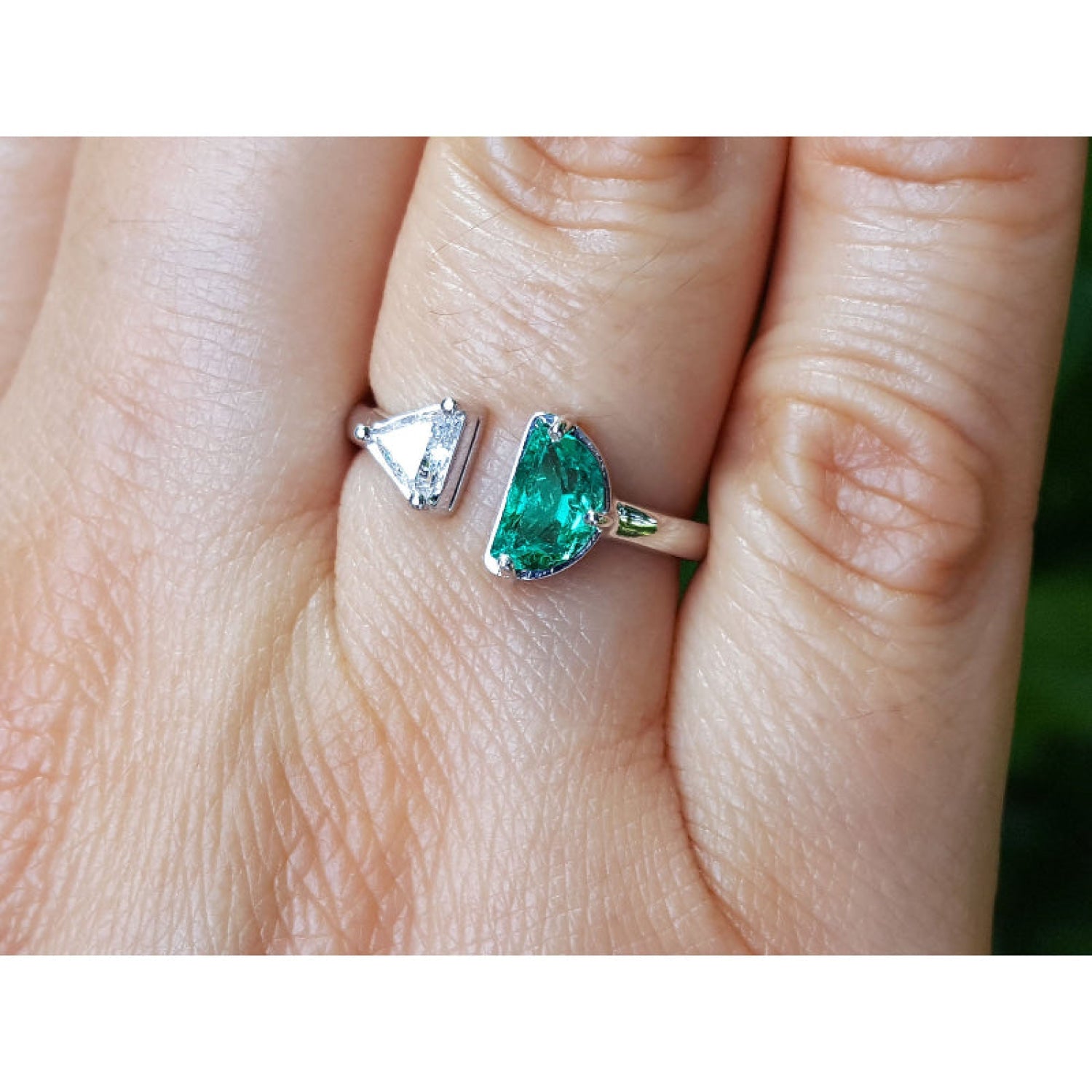 A close-up of a hand wearing a toi et moi emerald and diamond ring in white gold.