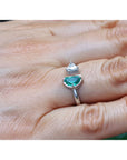 A negative space Toi et Moi ring features a half-moon-shaped natural Colombian emerald and a trillion-cut diamond, on a person's finger.