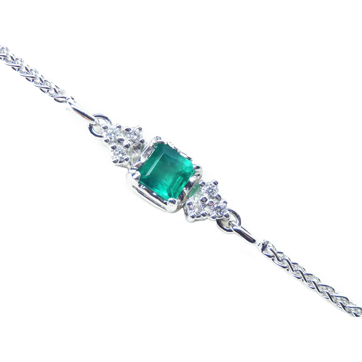 Topside view of a white gold bracelet with a square natural emerald and diamonds on a white background.