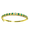 
the topside view of a gold bangle bracelet with round cut natural emeralds on a white background.