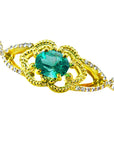 A topside view of a yellow gold bracelet with an oval cut natural emerald and accent diamonds.