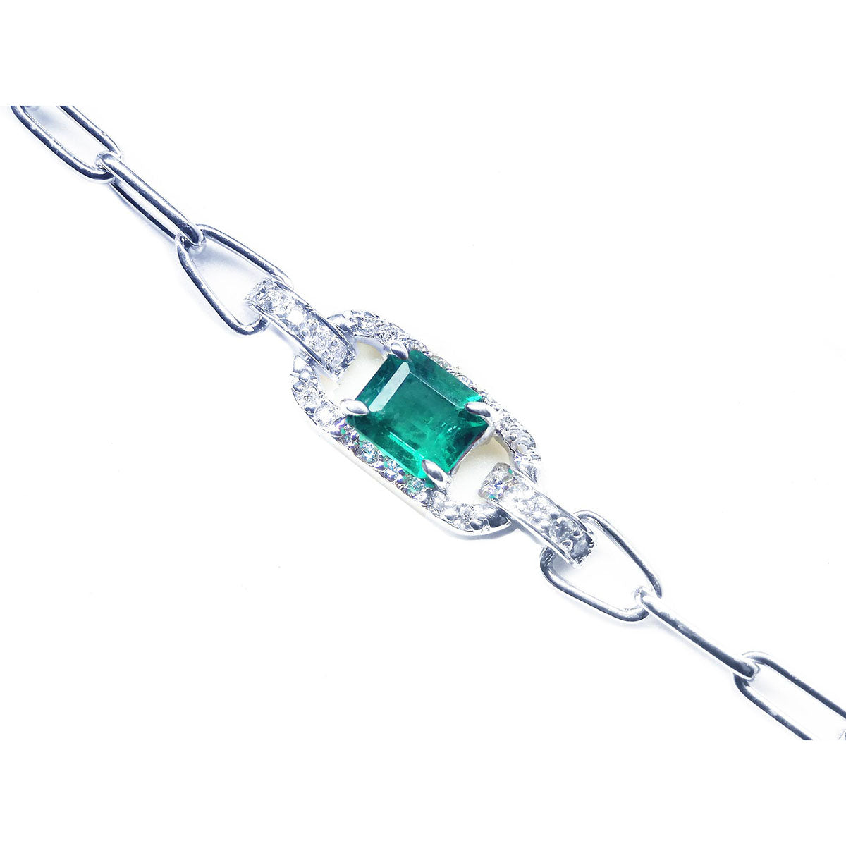 A white gold paperclip bracelet with a natural emerald and diamonds on a topside view.