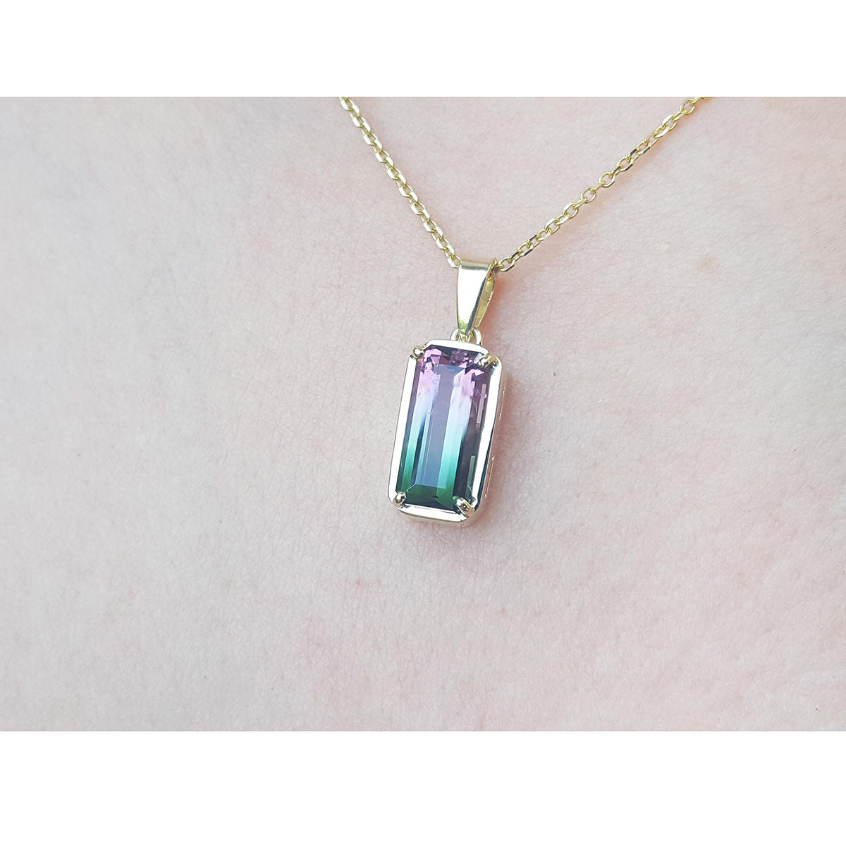 Multicolored gemstone tourmaline pendant on a gold chain against a light pink skin background.