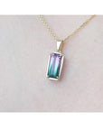 Multicolored gemstone tourmaline pendant on a gold chain against a light pink skin background.