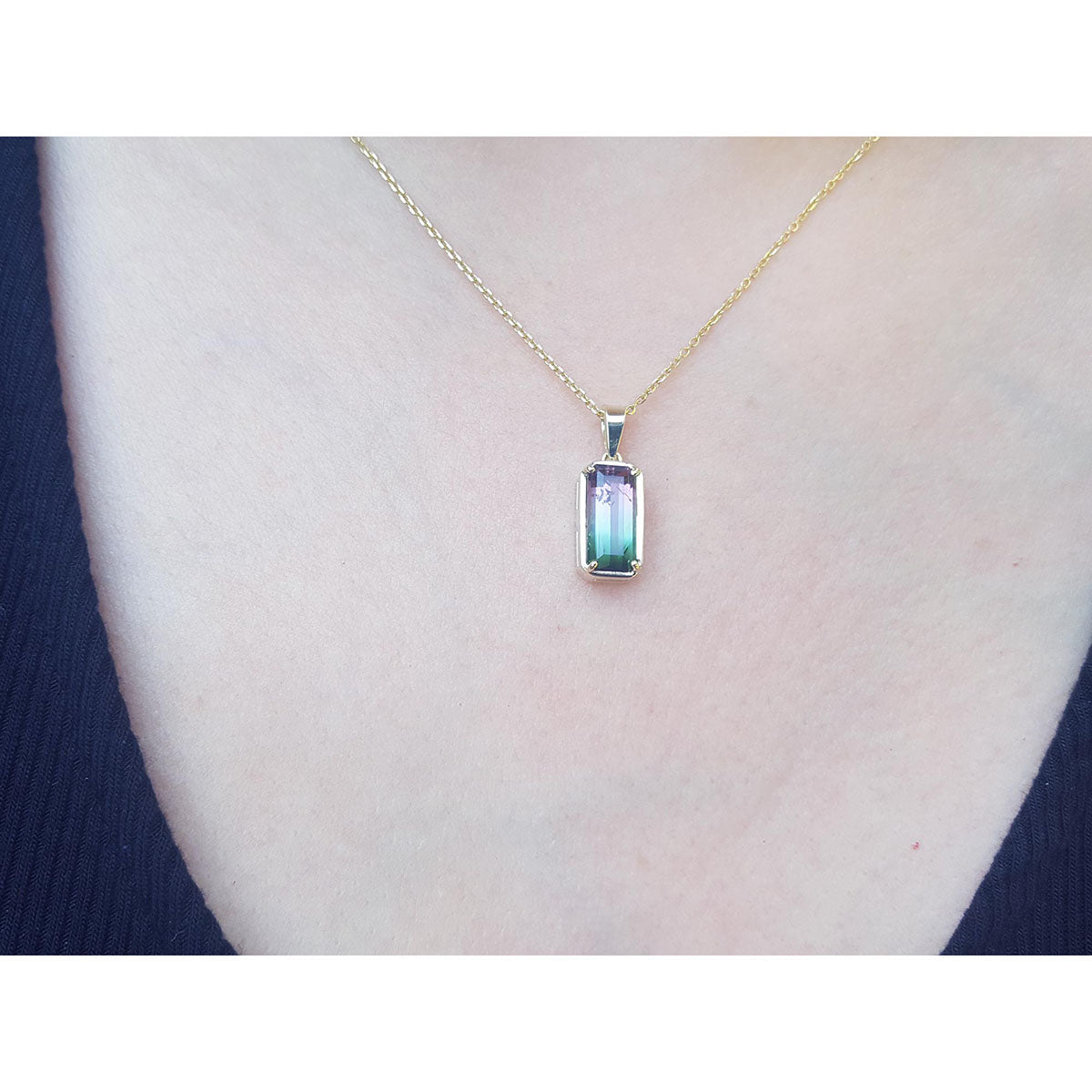 Gold necklace with a pendant featuring a multicolored tourmaline gemstone on a person&#39;s neck.
