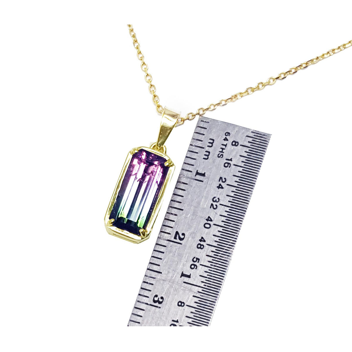 Gold necklace with a multicolored natural tourmaline gemstone pendant next to a ruler for scale on a white background.