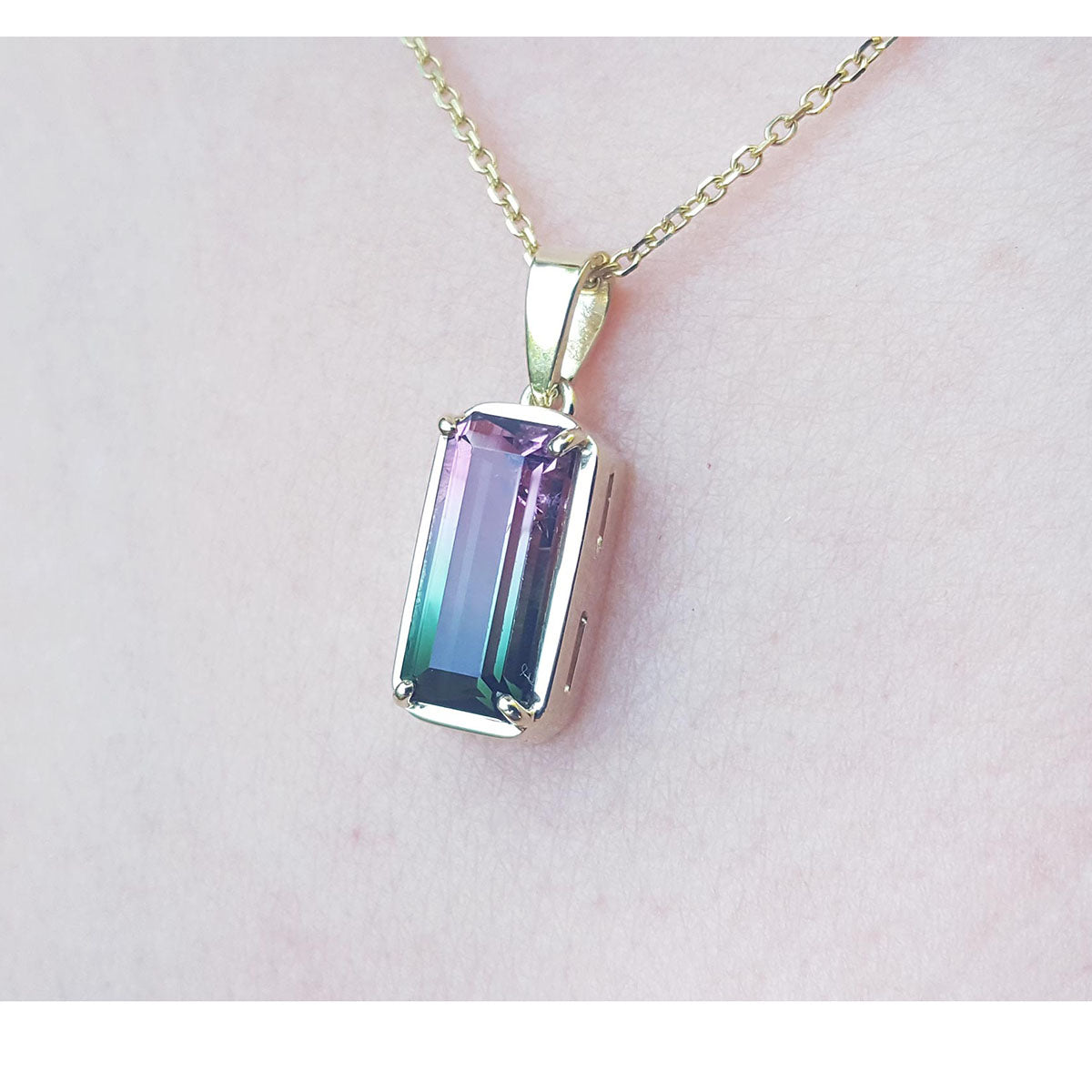 Necklace with a colorful tourmaline pendant on a light pink skin background.