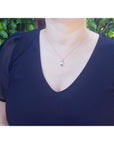 Person wearing a dark blue top with a tourmaline necklace against a green leafy background.