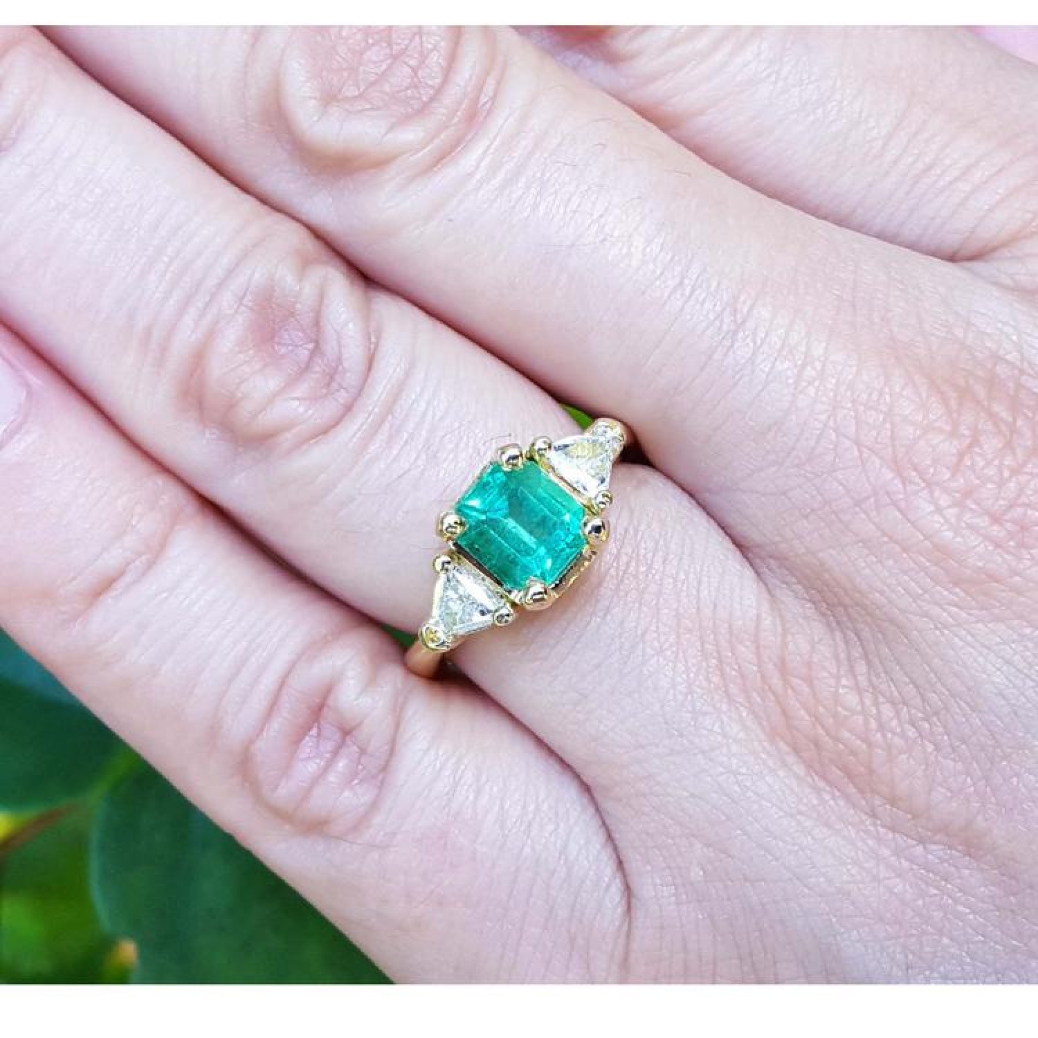 1.51 ct. emerald and trillion cut diamonds ring in 18k gold on a hand.