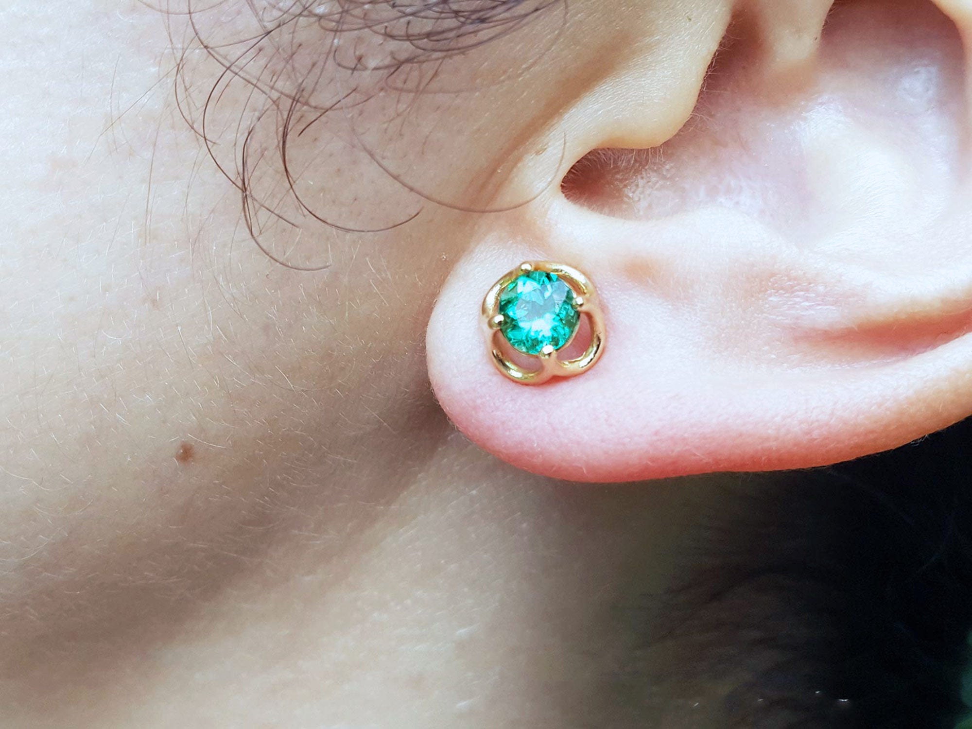 Close-up of an ear wearing a tulip emerald stud earring.