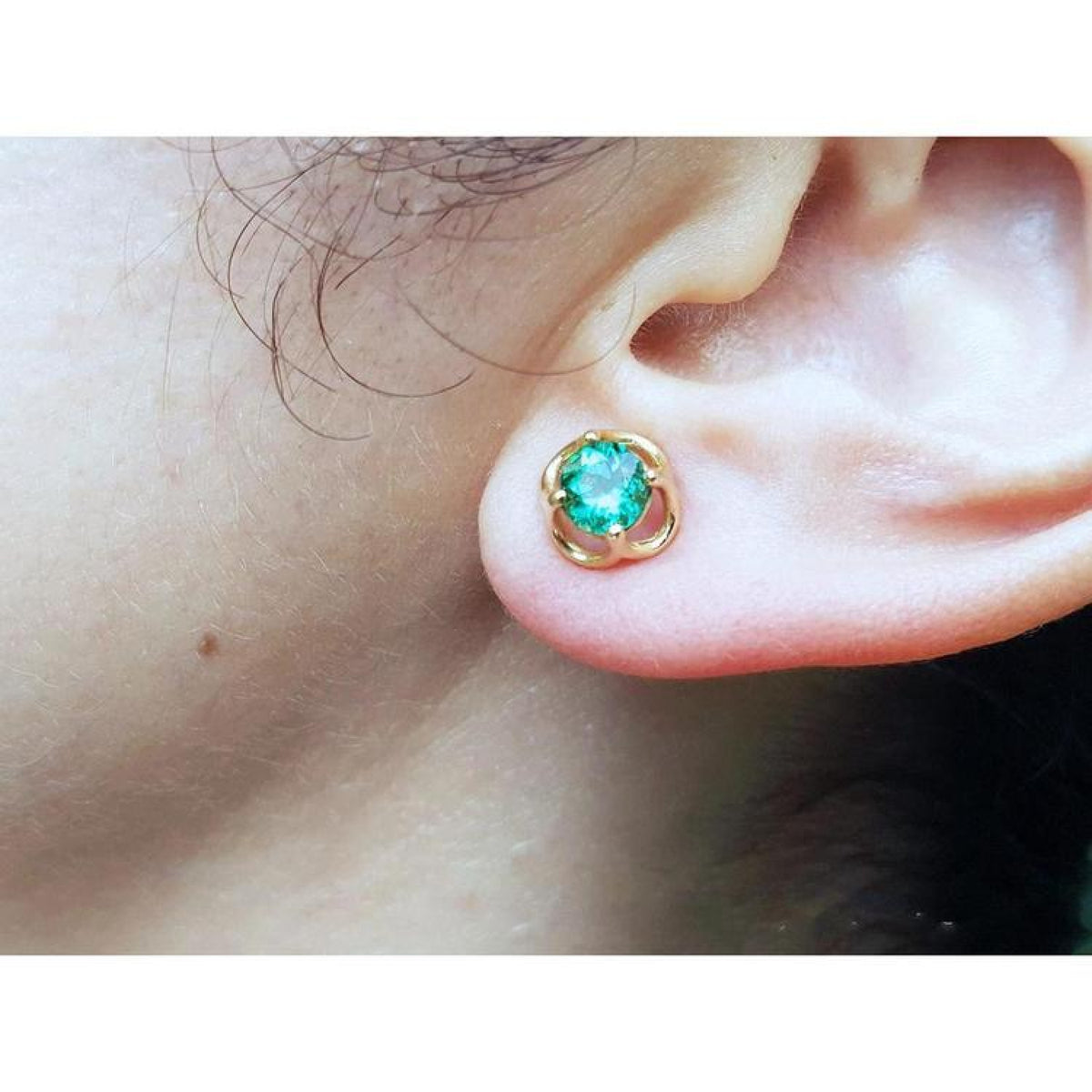 Close-up of an ear wearing a tulip natural emerald stud earring.