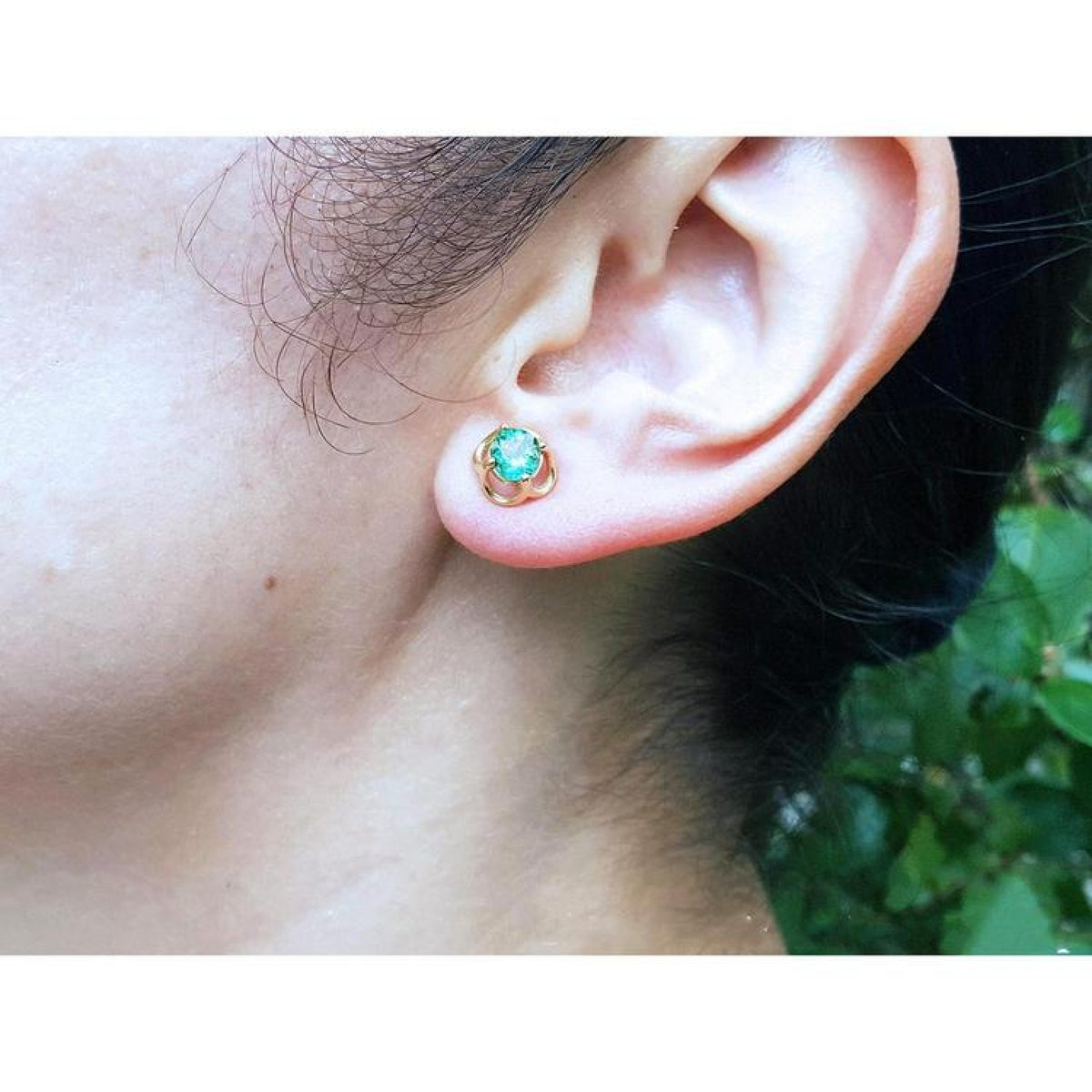 Colombian emerald tulip stud earrings in 14K yellow gold, worn on an ear.