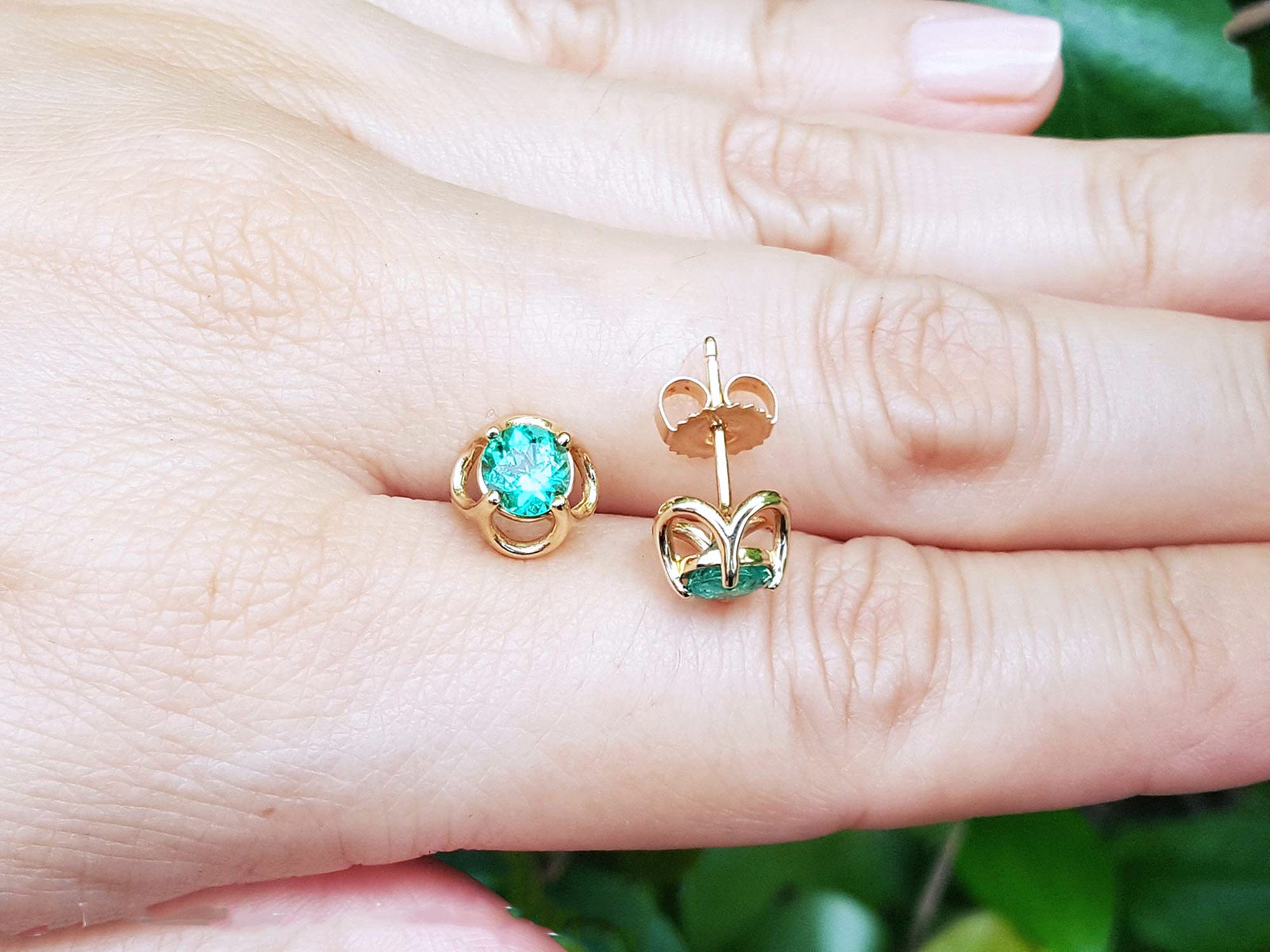 14k yellow gold tulip emerald stud earrings on a hand against a natural background.