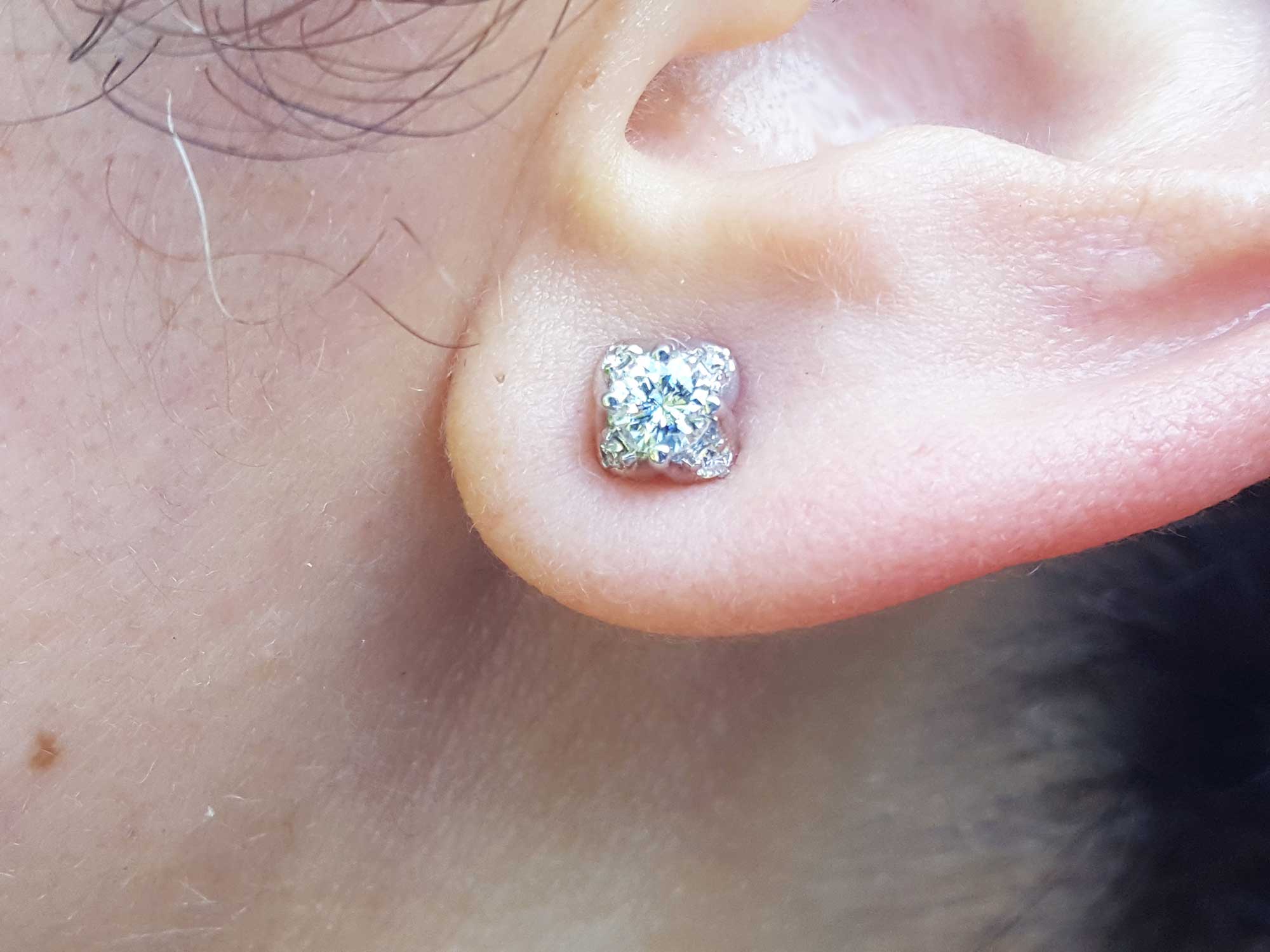 A woman's ear wearing a white gold diamond stud earring, tulip style.