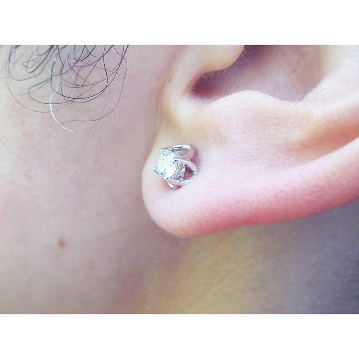 White gold tulip stud earring with a round natural diamond, worn on an ear.