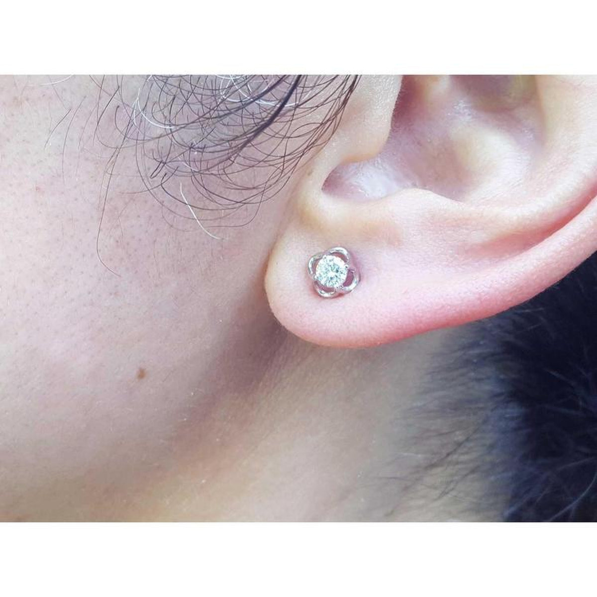 White gold tulip stud earring with a round diamond, worn on an ear.