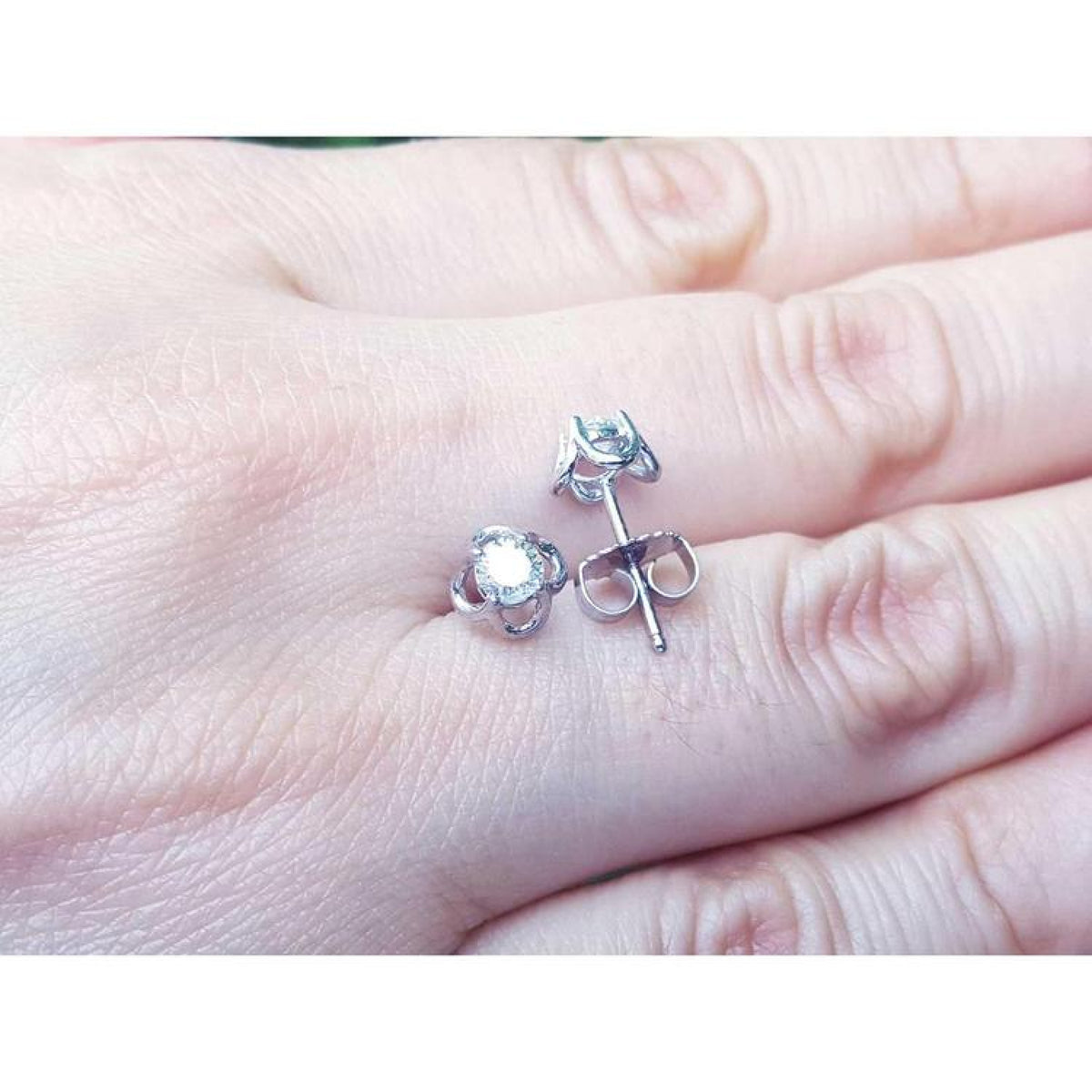 White gold natural diamond tulip stud earrings with round cut diamonds on a hand.