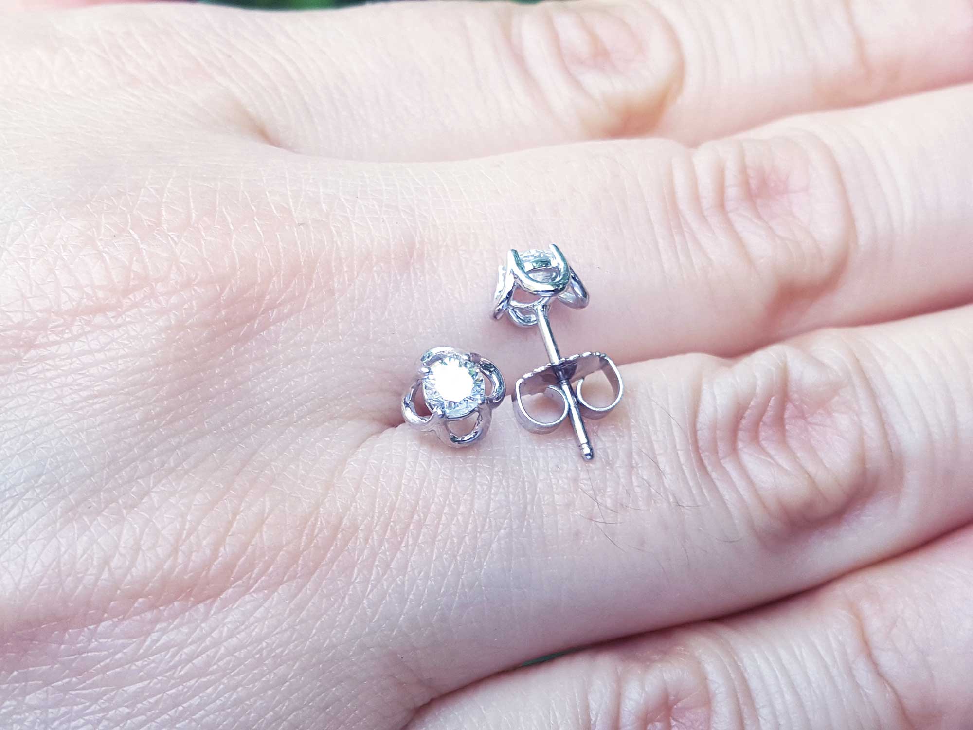 Displayed on a person&#39;s hand a pair of natural diamond tulip stud earrings, push backs.