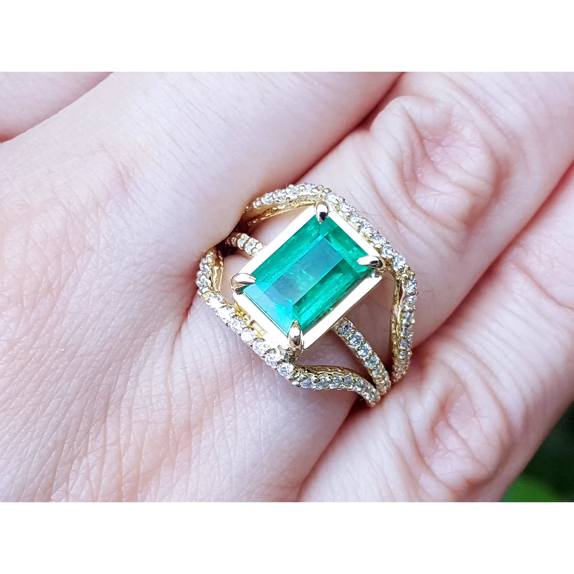 Toma grafica cercana de una mano exhibiendo un anillo de oro amarillo con esmeralda rectangular y diamantes laterales.