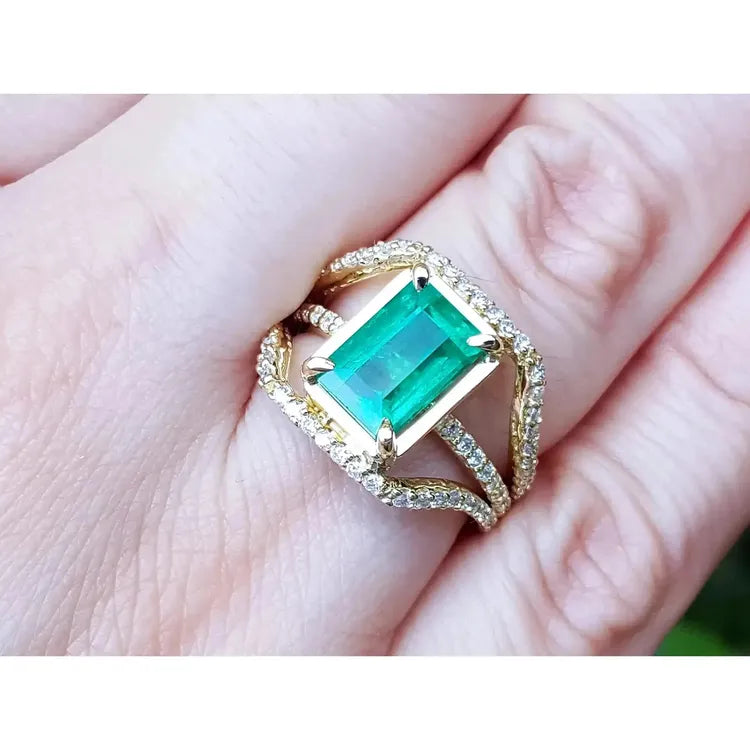 Toma grafica cercana de una mano exhibiendo un anillo de oro amarillo con esmeralda rectangular y diamantes laterales.