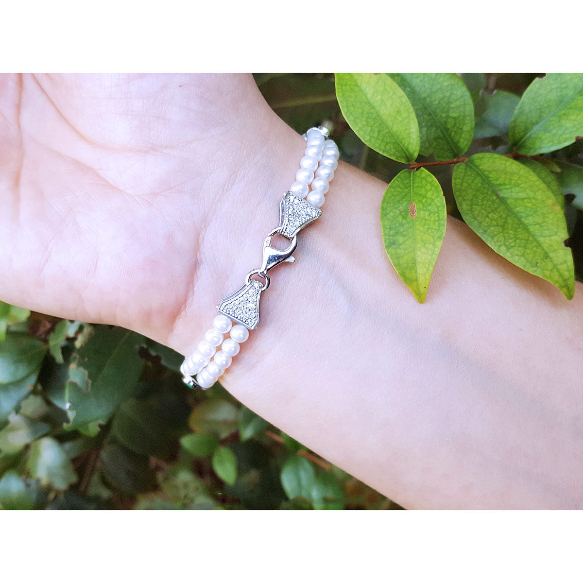 Pearl bracelet on a wrist with green leaves in the background.