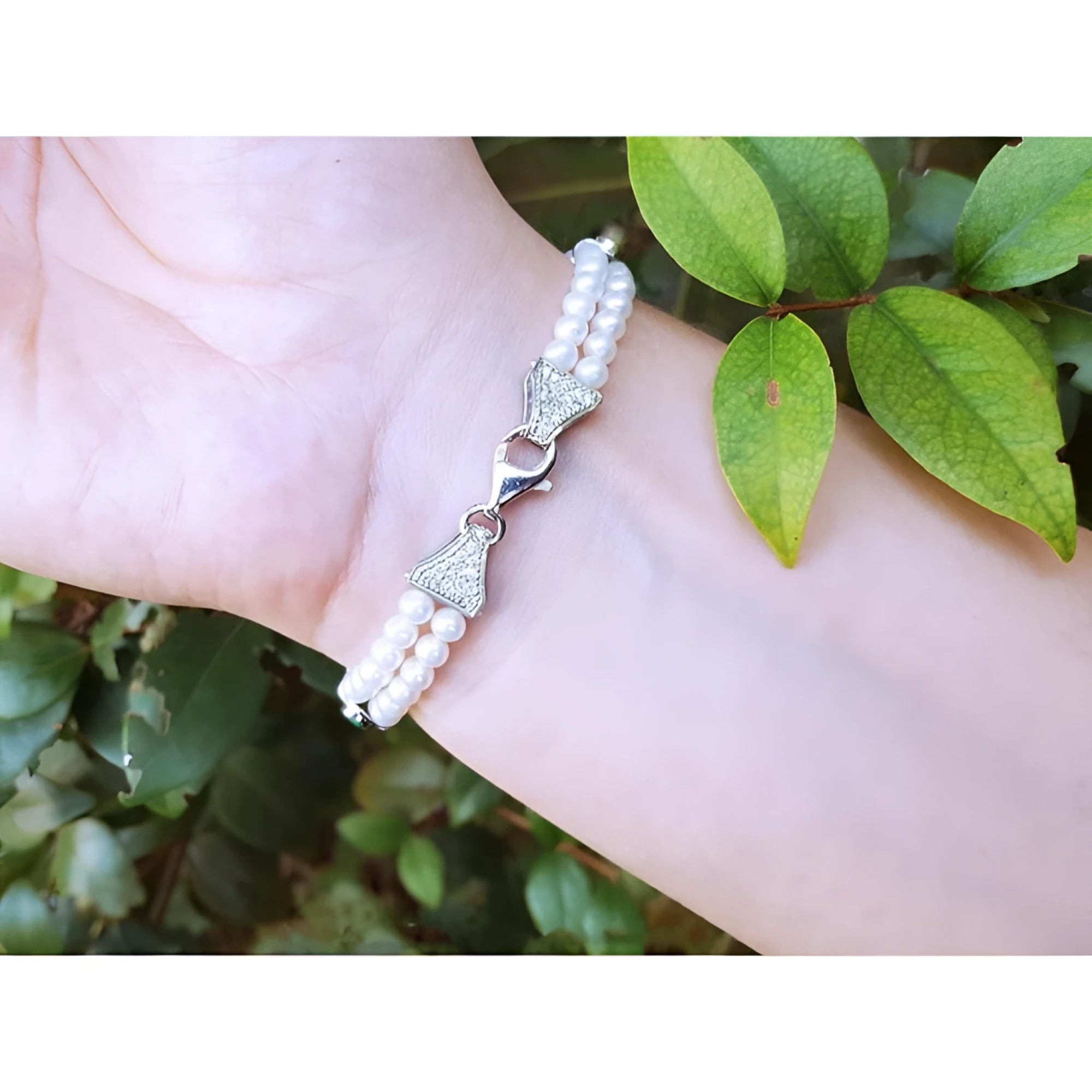18K white gold double-strand pearl bracelet with diamond-accented bow clasp on a wrist.
