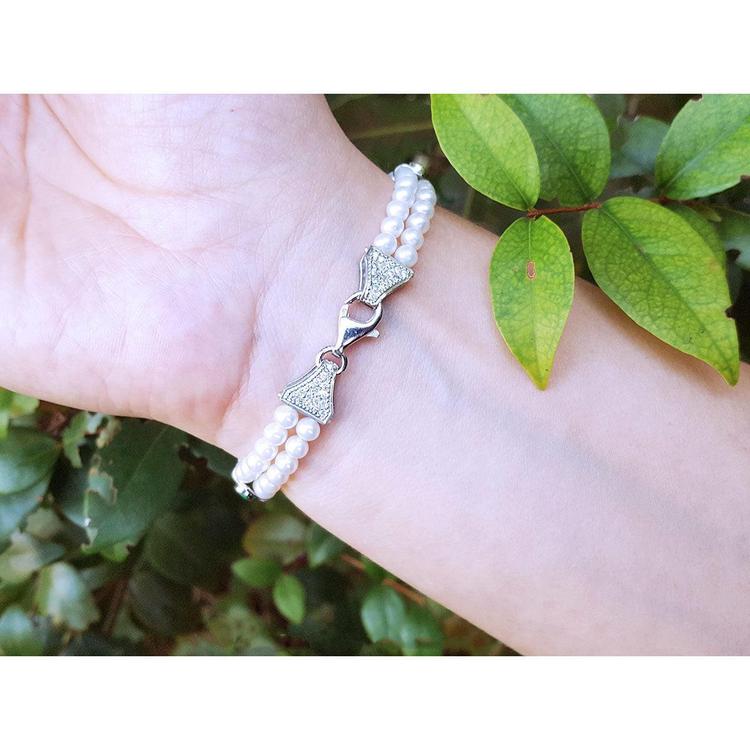 18K white gold double-strand pearl bracelet with diamond-accented bow clasp on a wrist.